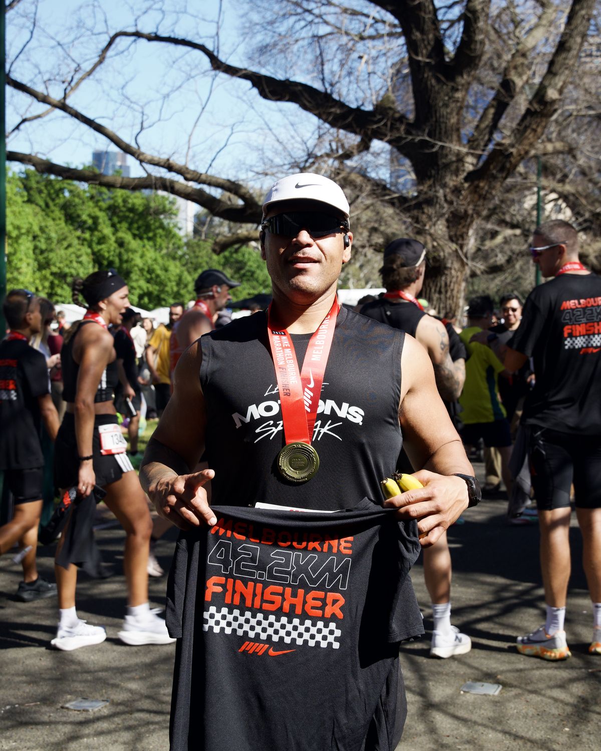 Marathon finisher holding up his Melbourne 42.2km finisher shirt, medal around his neck