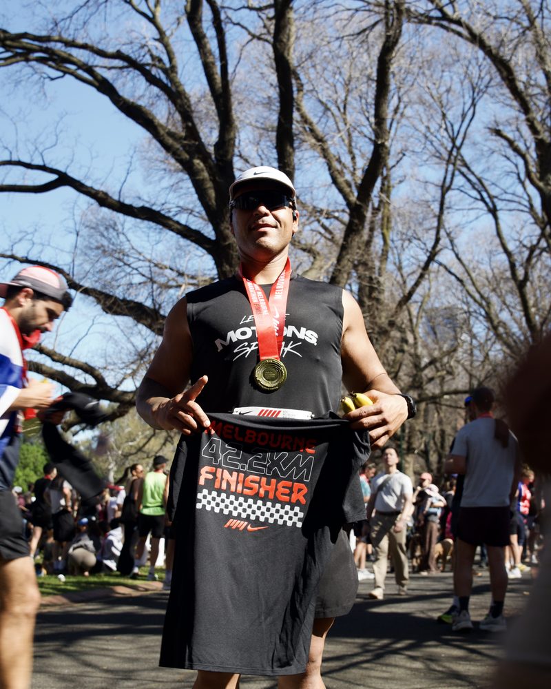 Runner holding up his Melbourne Marathon finisher shirt, medal around his neck